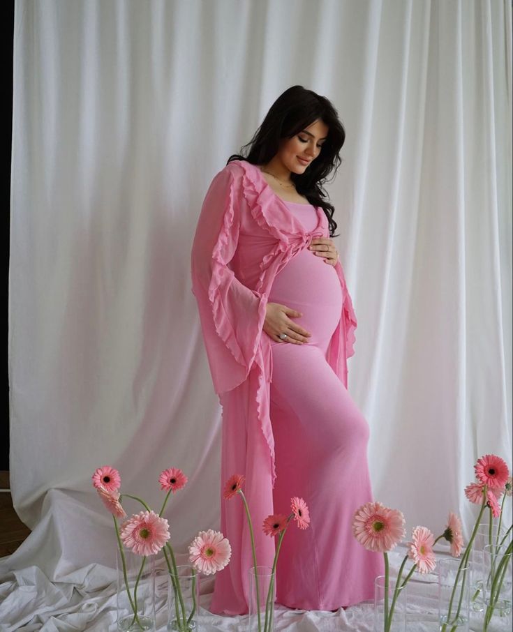 a pregnant woman in a pink gown standing next to flowers