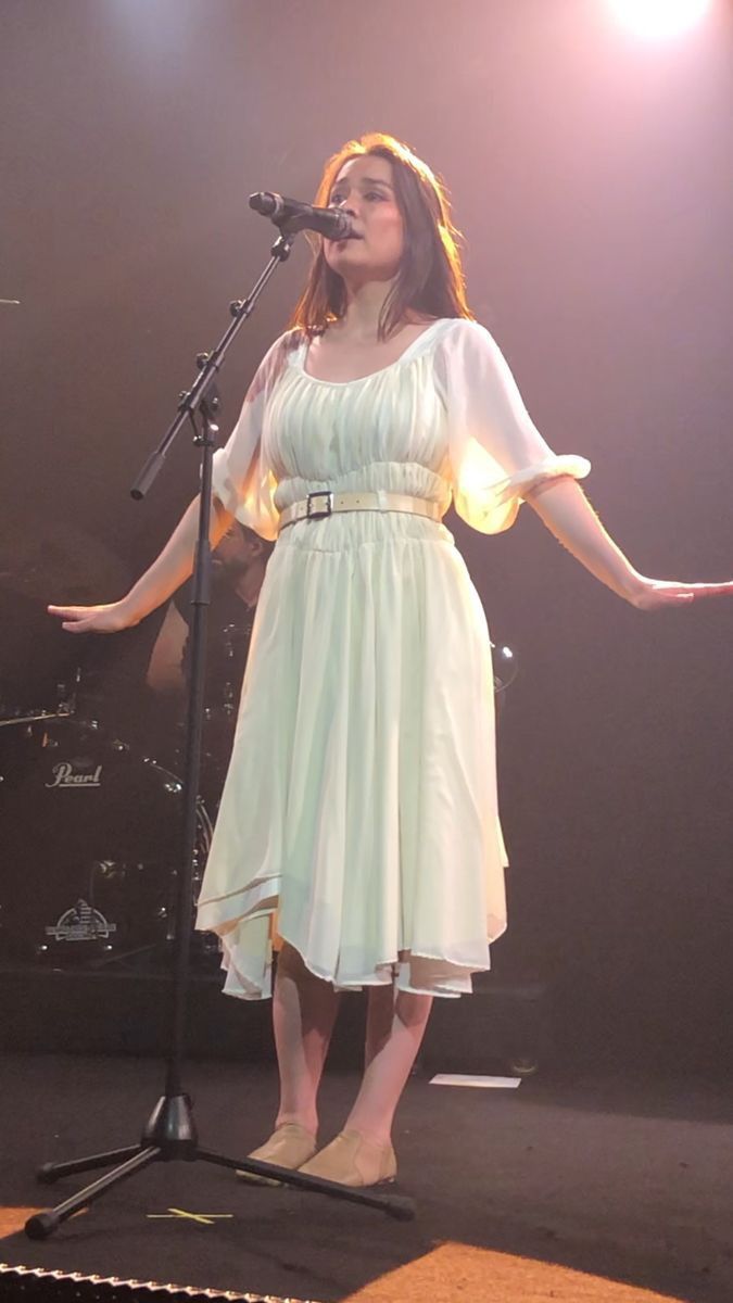 a woman in a white dress singing into a microphone