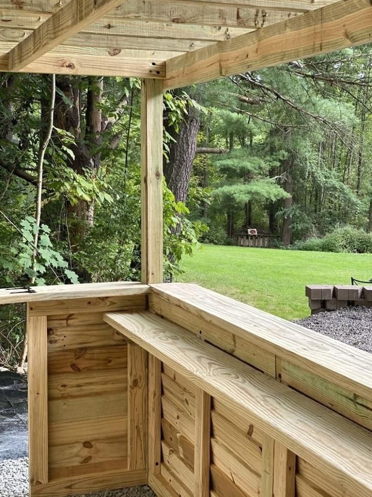 a wooden bench sitting on top of a lush green field next to a forest filled with trees