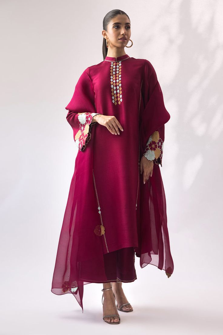 A berry rawsilk kurta with floral appliqué work placed on the sleeve cuffs is a bright summer outfit choice. It is paired with tonal rawsilk culottes and an organza dupatta, embellished with colorful appliqué flowers around the edges, creating a coordinated look. Eid Straight Kurta In Organza, Cotton Silk Lawn Suit For Party With Straight Kurta, Organza Palazzo Set With Dabka Detail, Party Cotton Silk Lawn Suit With Straight Kurta, Festive Straight Organza Kurta, Summer Festive Organza Kurta, Summer Festive Organza Palazzo Set, Silk Kurta With Sheer Dupatta For Eid, Elegant Cotton Silk Salwar Kameez With Embroidered Sleeves