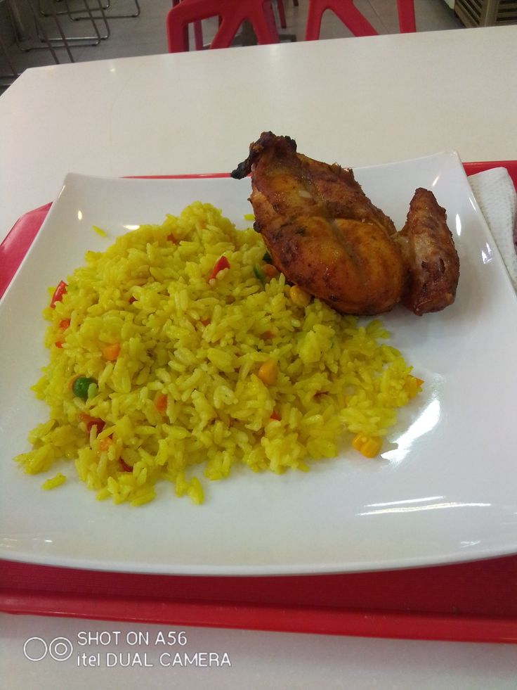 a white plate topped with rice and meat next to a red tray on a table