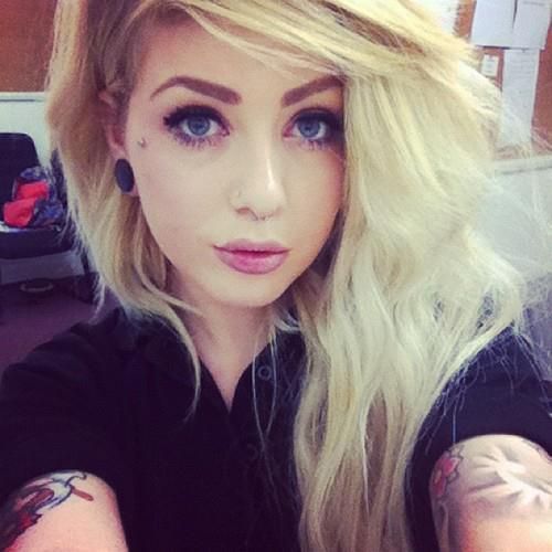 a woman with long blonde hair and tattoos on her arm looking at the camera while she is taking a selfie