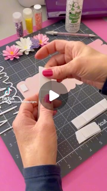 a woman is cutting paper with scissors on a pink table top and another person is holding a piece of paper