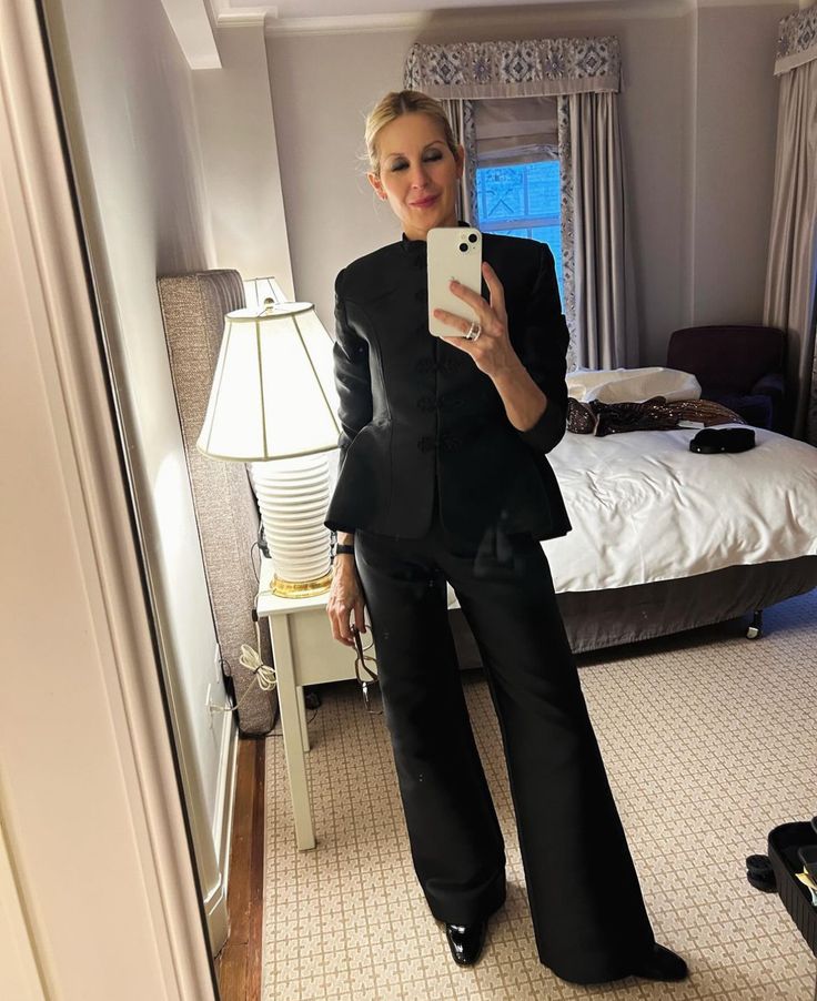 a woman is taking a selfie in her hotel room while wearing black pants and a blazer