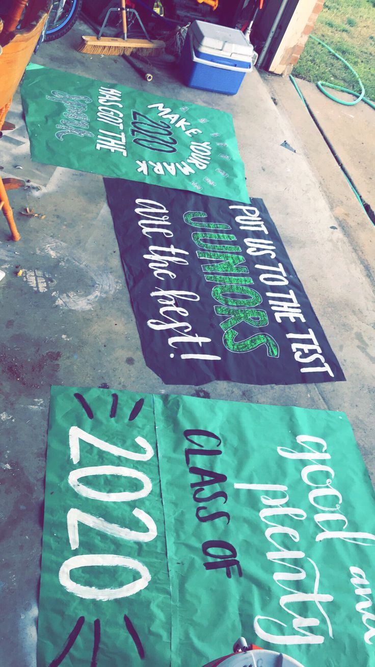 three green banners with white writing are on the sidewalk next to chairs and trash cans