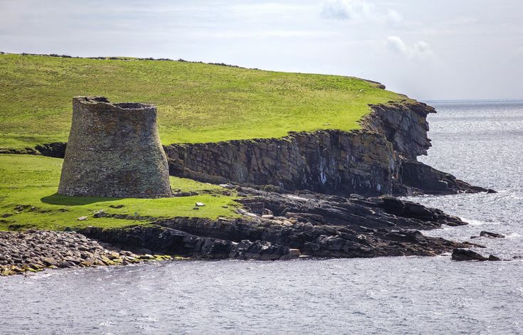 an old stone tower on the edge of a cliff by the water's edge