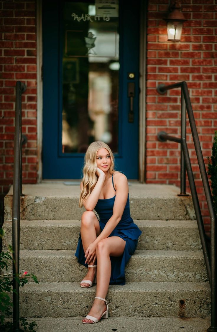 a beautiful blonde woman sitting on steps in front of a blue door with her legs crossed