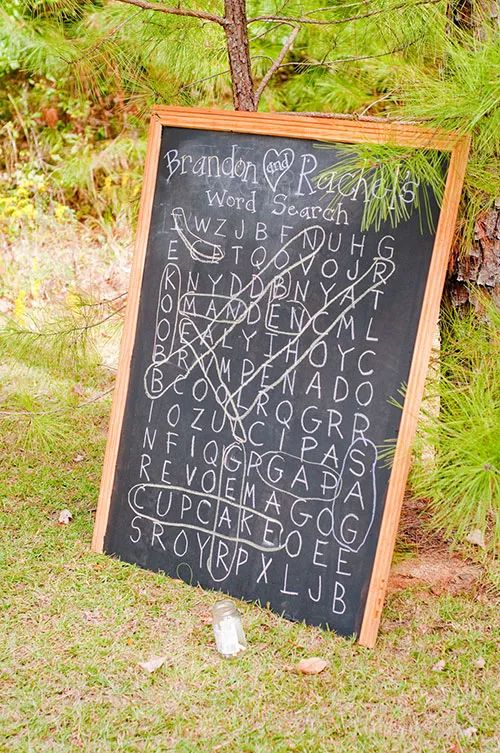 a chalkboard sign sitting in the grass next to a pine tree with writing on it