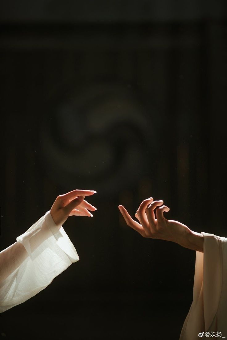 two hands reaching out towards each other in front of a dark background with the light shining on them