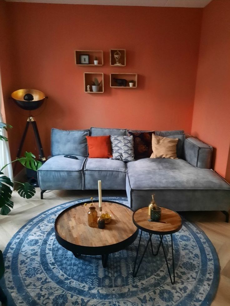 a living room with an orange wall and blue rug on the floor, two couches in front of a round coffee table