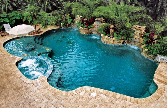 a swimming pool surrounded by palm trees and other greenery, with an umbrella in the middle