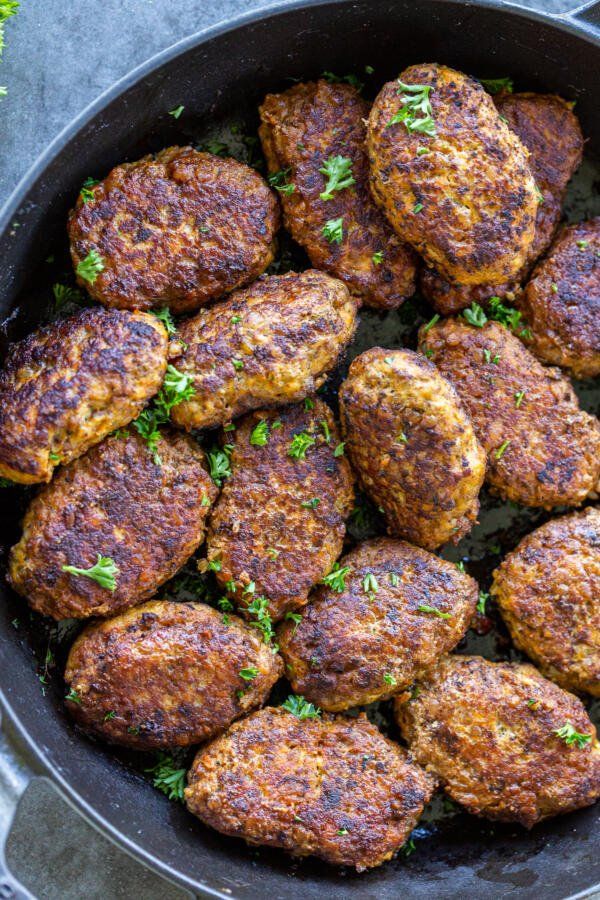 some meat patties in a pan with parsley on the top and seasoning