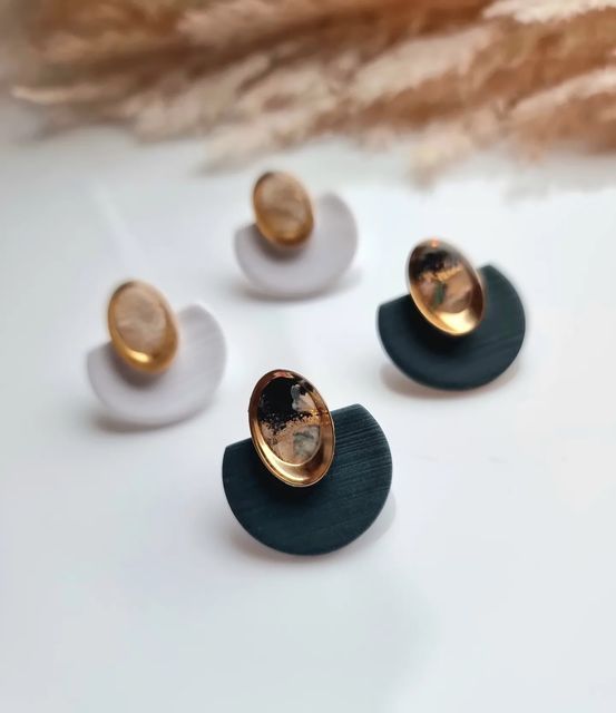 three pairs of earrings with gold and black designs on them sitting on a white surface