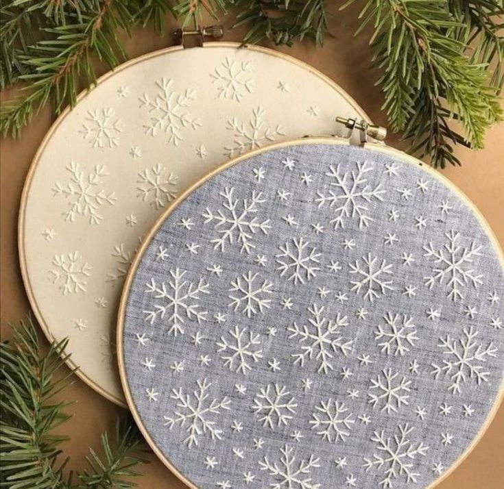 two embroidery hoops with snowflakes on them hanging from a christmas tree branch