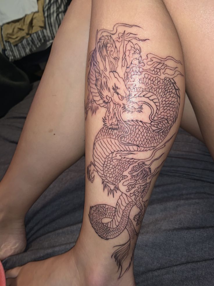 a woman's leg with a dragon tattoo on it, sitting on a bed