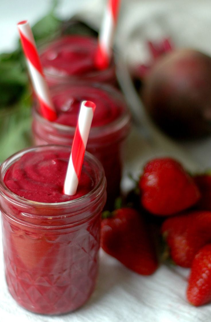 three mason jars with strawberries in them sitting on a table next to some fruit