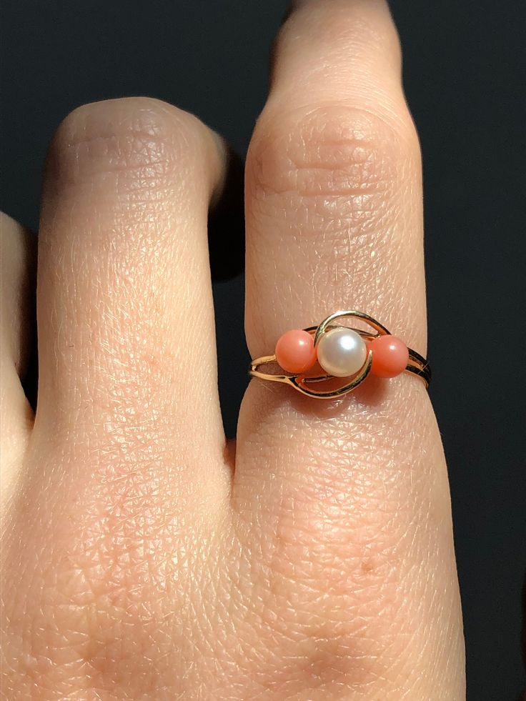 Vintage 14k gold ring with a centre pearl and two coral balls on either side. The coral varies slightly in colour which is normal for natural coral. Stamped and tested 14k gold. In great condition with minimal signs of wear. Very delicate in style and design.  Fits US ring size 6 (measures just a touch over a size 6) Design is 8 mm wide on the finger at the widest part The pearl is approximately 3 mm wide 1.2 grams in weight Will be mailed with tracking and in a gift box! Coral Gemstone Jewelry For Weddings, Vintage Coral Rings As A Gift, Coral Rings For Women, Elegant Coral Ring Jewelry, Coral Rings, Coral Stone Ring, Trilogy Ring, Coral Ring, Solid Gold Ring