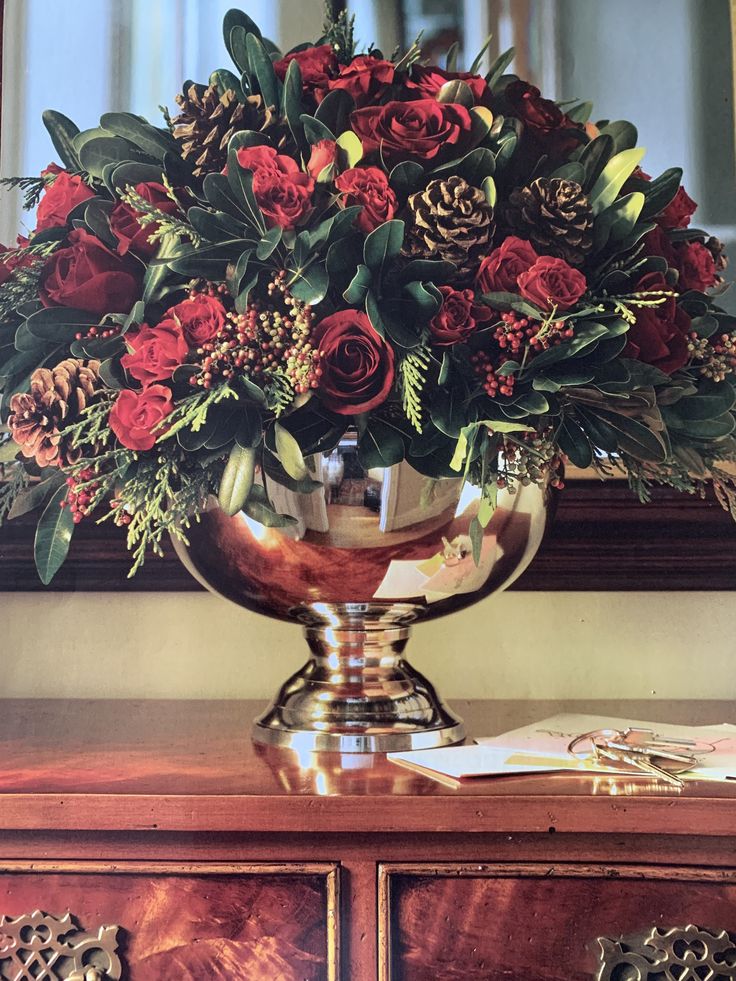 a vase filled with red flowers sitting on top of a wooden dresser next to a mirror