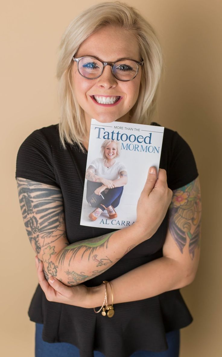 the tattooed woman is holding her book in front of her face and smiling at the camera