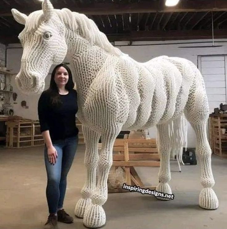 a woman standing next to a large white horse made out of plastic straws in a warehouse