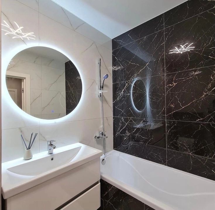 a bathroom with black marble walls and white fixtures, along with a round mirror above the bathtub