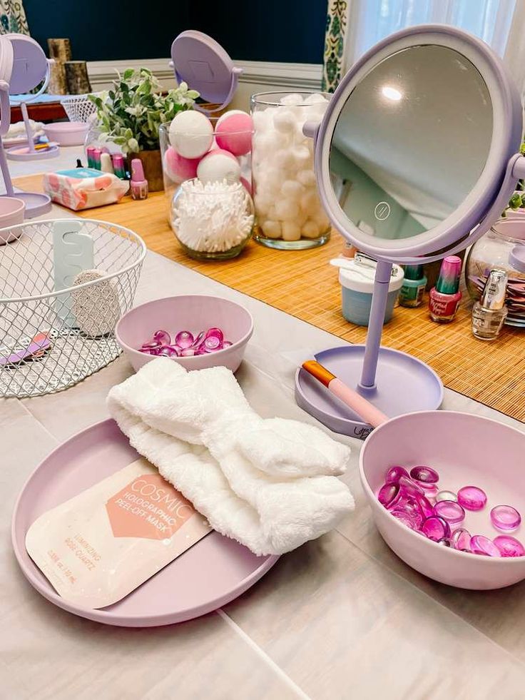 a table topped with lots of pink bowls filled with candy and other items next to a mirror