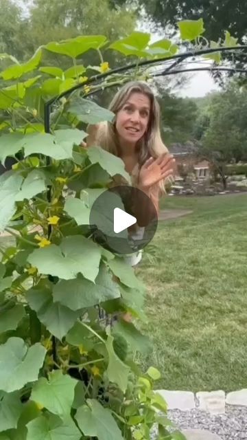 a woman standing next to a green plant in a garden with lots of leaves on it