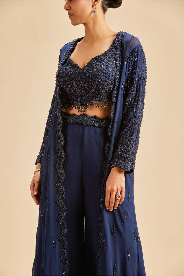 Editor's Note Navy blue georgette sharara with blouse and long jacket embroidered in tonal sequins, beadwork and crystals Color: Blue Fabric: Georgette and net Components: Sharara, blouse and jacket Occasion: Wedding guest Disclaimer: Product color may slightly vary due to photographic lighting sources or your monitor setting. Care: Dry Clean Only About the Designer Nitika Gujral’s journey with designing clothes started almost four decades back while she was still in high school and held her fir Blue Sharara, Blouse Yoke, Open Front Jacket, Sharara Set, Embroidered Jacket, How To Make Clothes, Cut Work, Embroidered Blouse, Wedding Wear