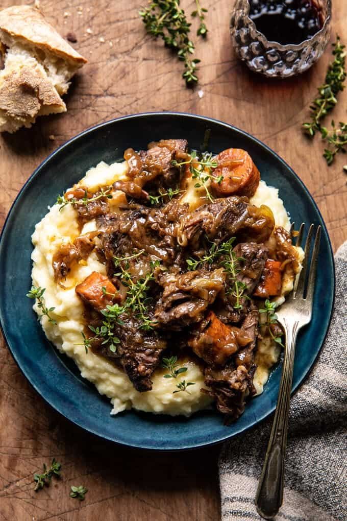 a blue plate topped with mashed potatoes covered in beef and carrots next to a glass of wine