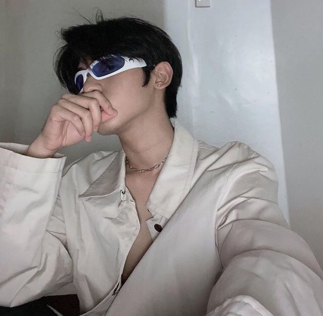 a man in white shirt and sunglasses sitting on the floor with his hand under his chin