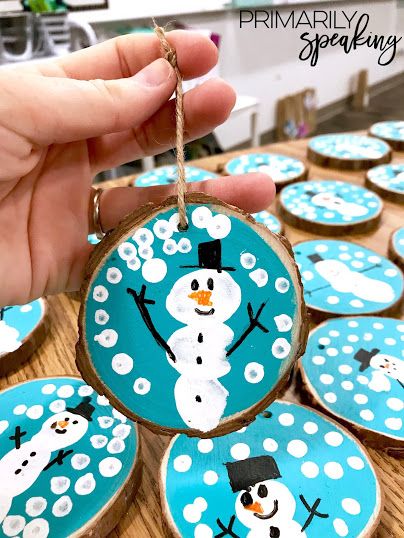 a hand holding a piece of wood with snowmen painted on it and hanging from strings