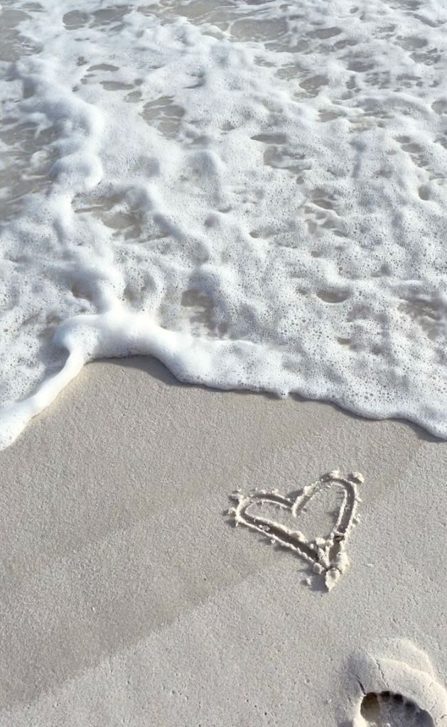 a heart drawn in the sand at the beach with waves lapping on it's shore