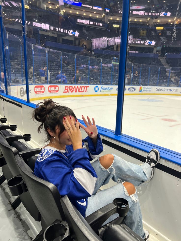 a woman is sitting on the bench at an ice hockey rink and covering her face