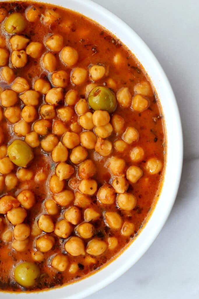 a white bowl filled with chickpeas and olives on top of a table