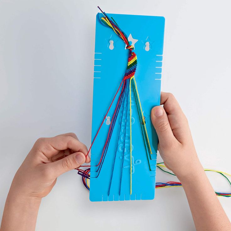 two hands are holding a piece of blue paper with colorful string attached to it while another hand holds the string