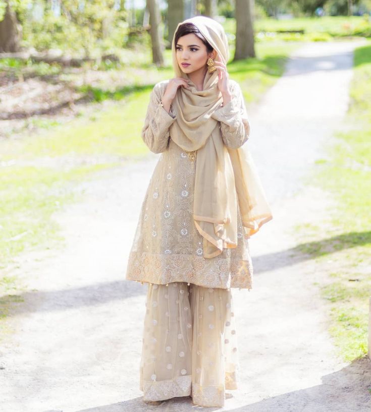 a woman standing on a path wearing a hijab and holding her hand up to her ear