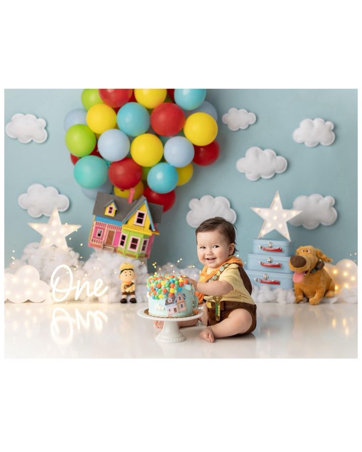 a baby is sitting in front of a cake with balloons on the wall behind it