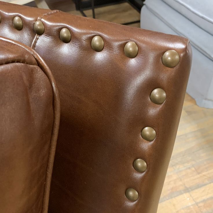 a brown leather couch with rivets and buttons on the armrest, in a living room