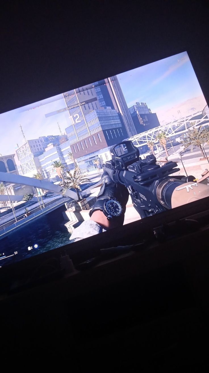 a person holding a video game controller in front of a large screen with cityscape on it