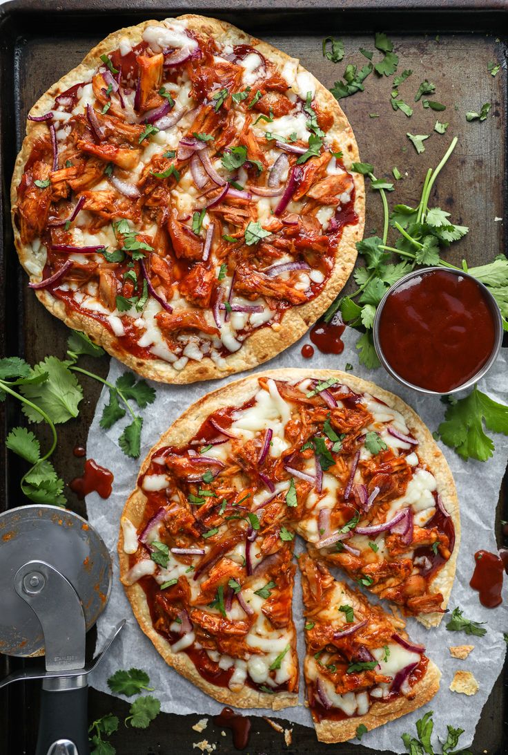 two pizzas sitting on top of a pan covered in sauce and garnish