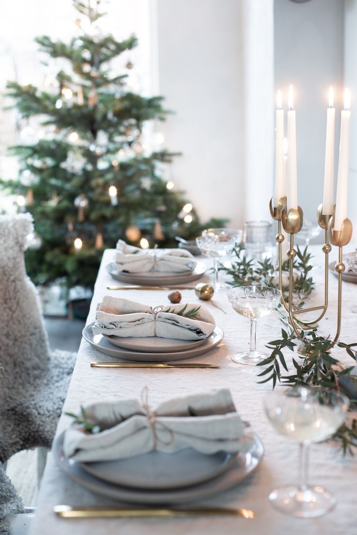 the table is set for christmas dinner with candles and plates on it, along with silverware