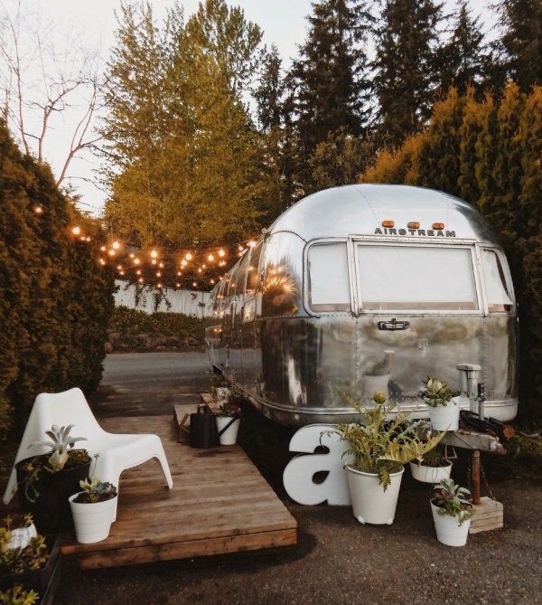 an airstream with lights and potted plants in the back yard is surrounded by greenery