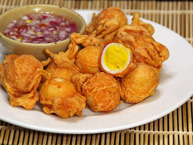 some fried food on a white plate with a bowl of dipping sauce