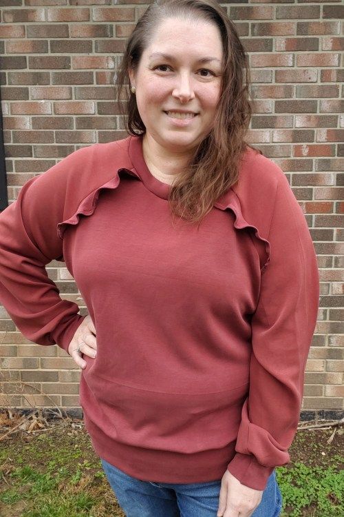 a woman standing in front of a brick wall wearing jeans and a red shirt with ruffles