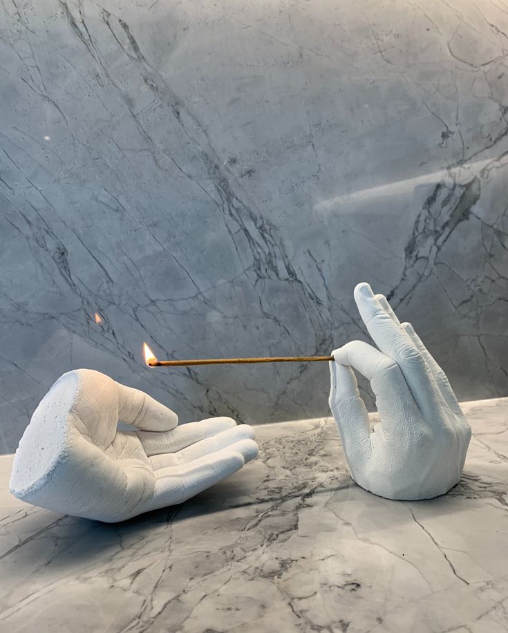 two hands holding a lit matchstick in front of a marble wall