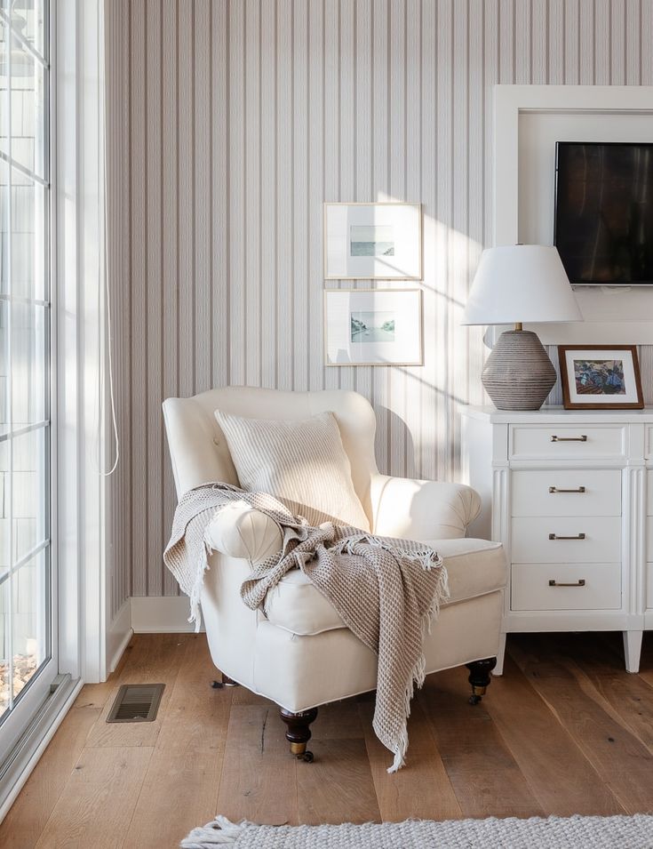 a white chair with a blanket on it in front of a window and a television