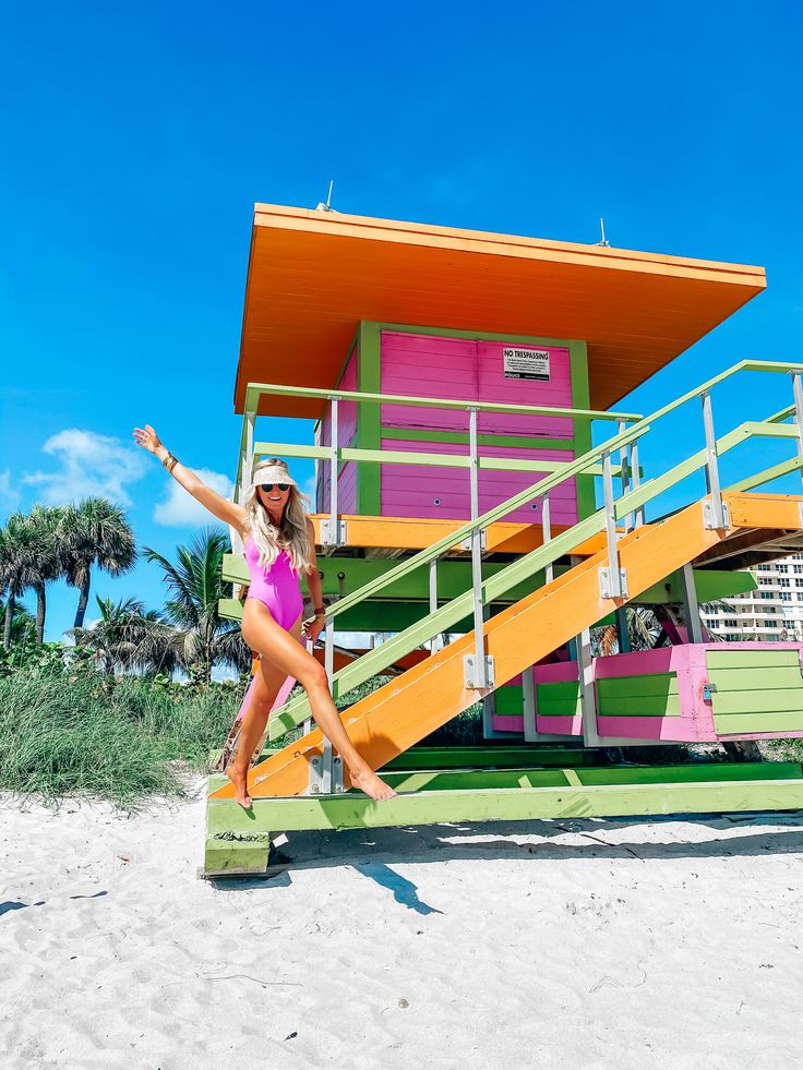 a woman in a pink swimsuit standing next to a lifeguard tower on the beach