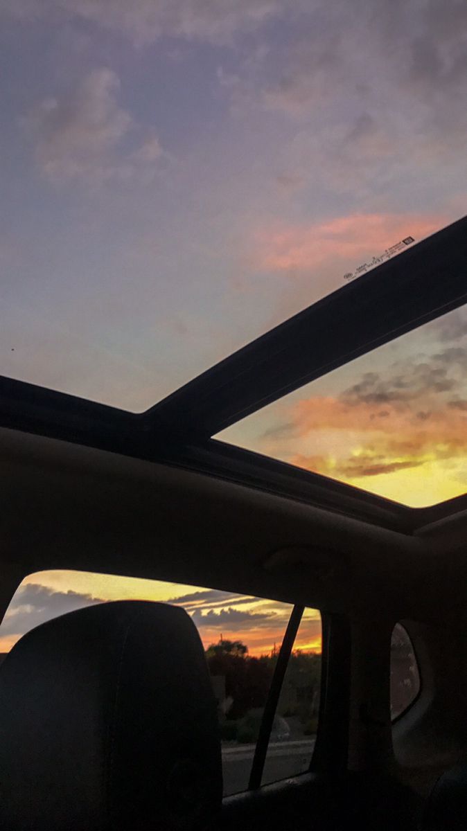 the sun is setting behind some clouds in the sky as seen from inside a car