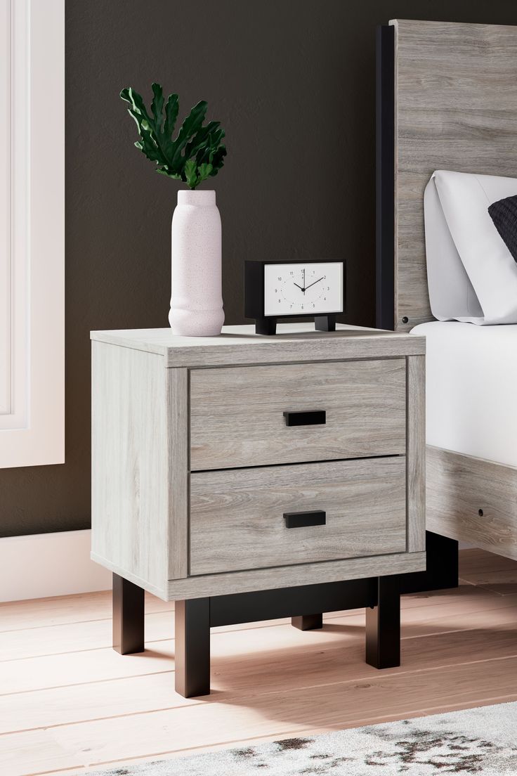 a bedroom scene with focus on the bedside table and bed in the foreground, along with a potted plant