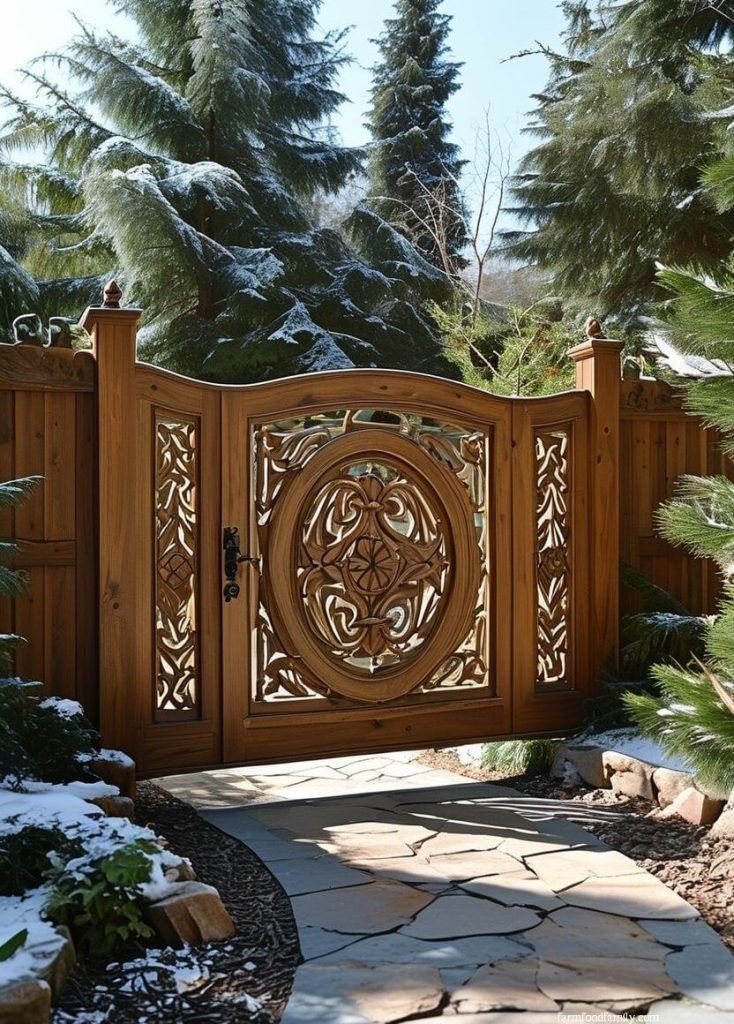 a wooden gate in the middle of a garden with snow on the ground and pine trees behind it